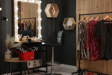Photo of Makeup room. Stylish mirror near dressing table, chair and clothes rack indoors