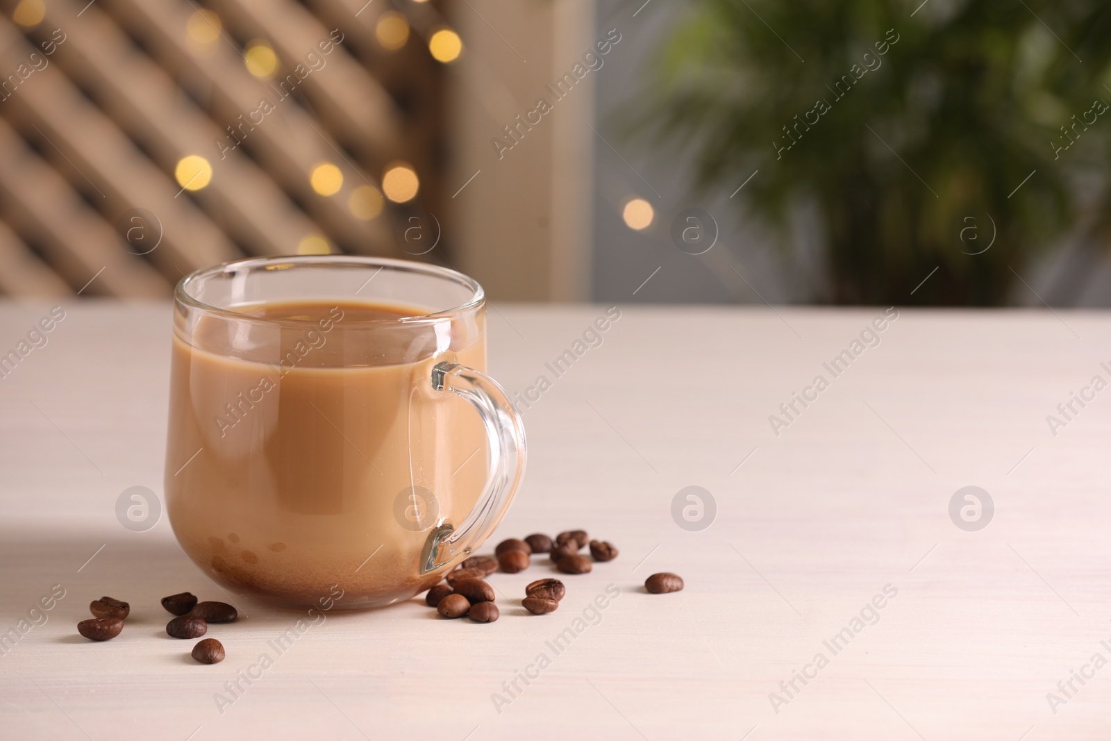Photo of Delicious coffee with milk in cup and beans on white wooden table. Space for text