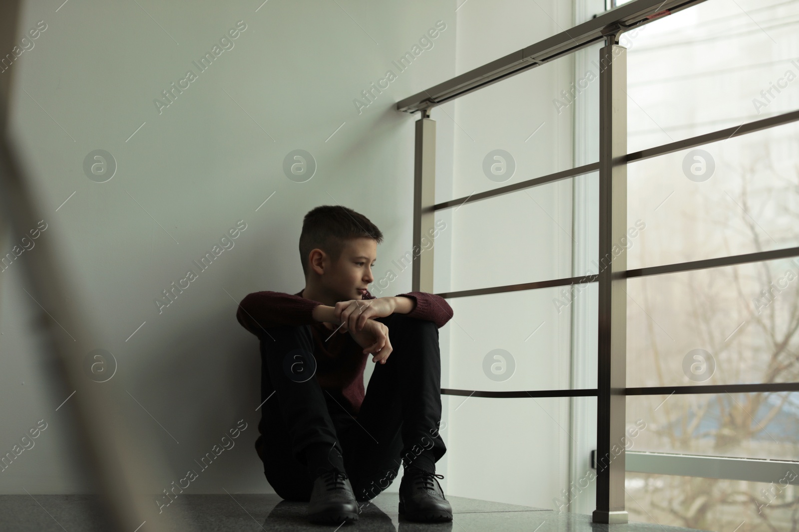 Photo of Upset boy sitting on staircase indoors. Space for text