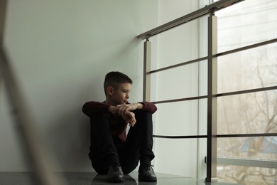 Upset boy sitting on staircase indoors. Space for text