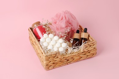 Photo of Spa gift set of different luxury products in wicker basket on pale pink background