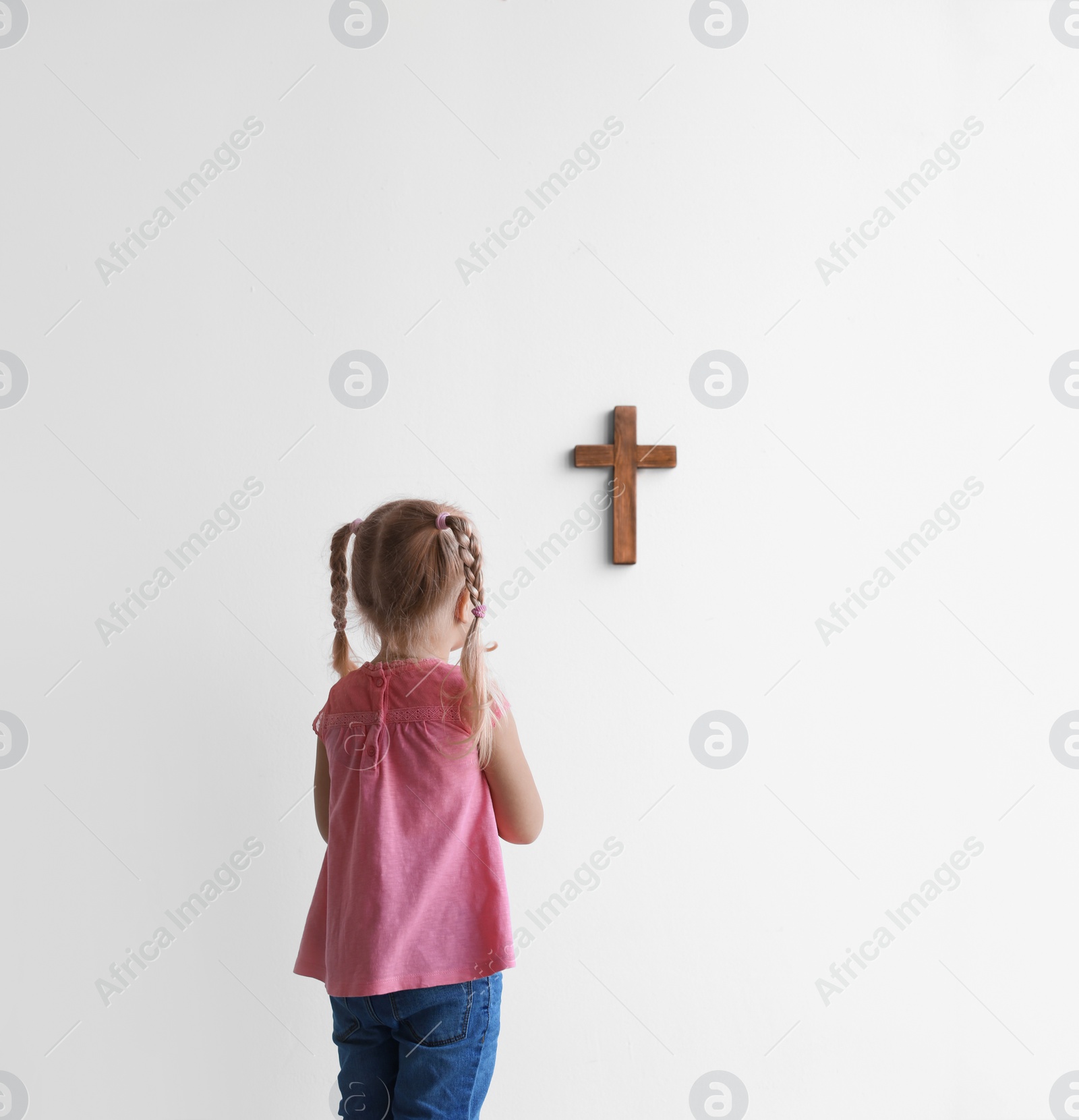 Photo of Little girl praying near light wall with cross