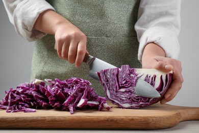 Photo of Woman cutting fresh radicchio cabbage on board at wooden table, closeup