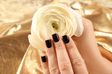 Photo of Woman with black manicure holding beautiful flower on golden background, closeup. Nail polish trends