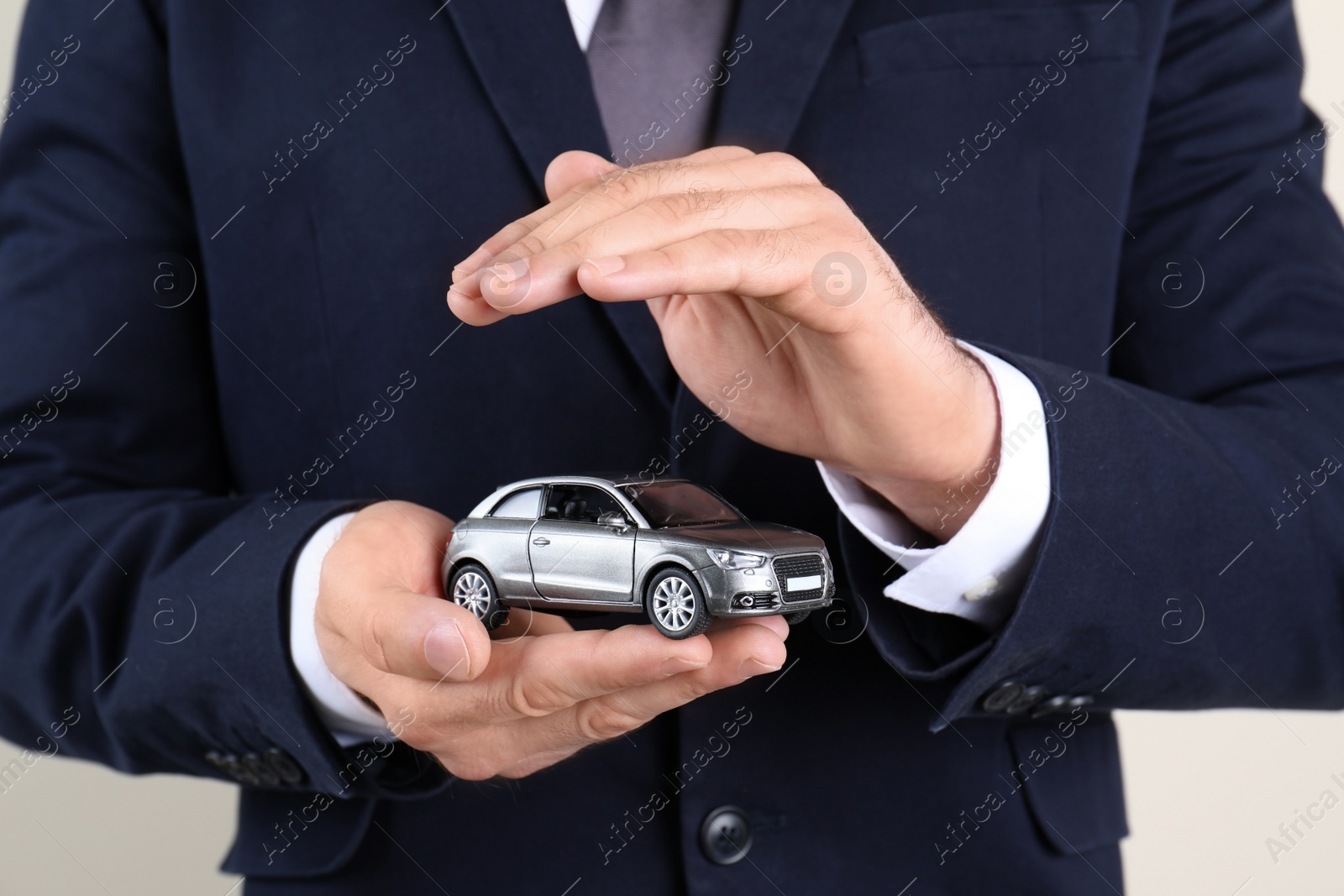 Photo of Male insurance agent holding toy car on light background, closeup