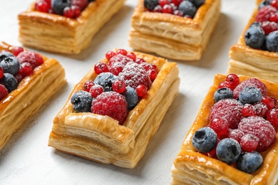 Fresh delicious puff pastry with sweet berries on light table, closeup