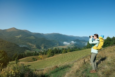 Photo of Tourist with hiking equipment looking through binoculars in mountains