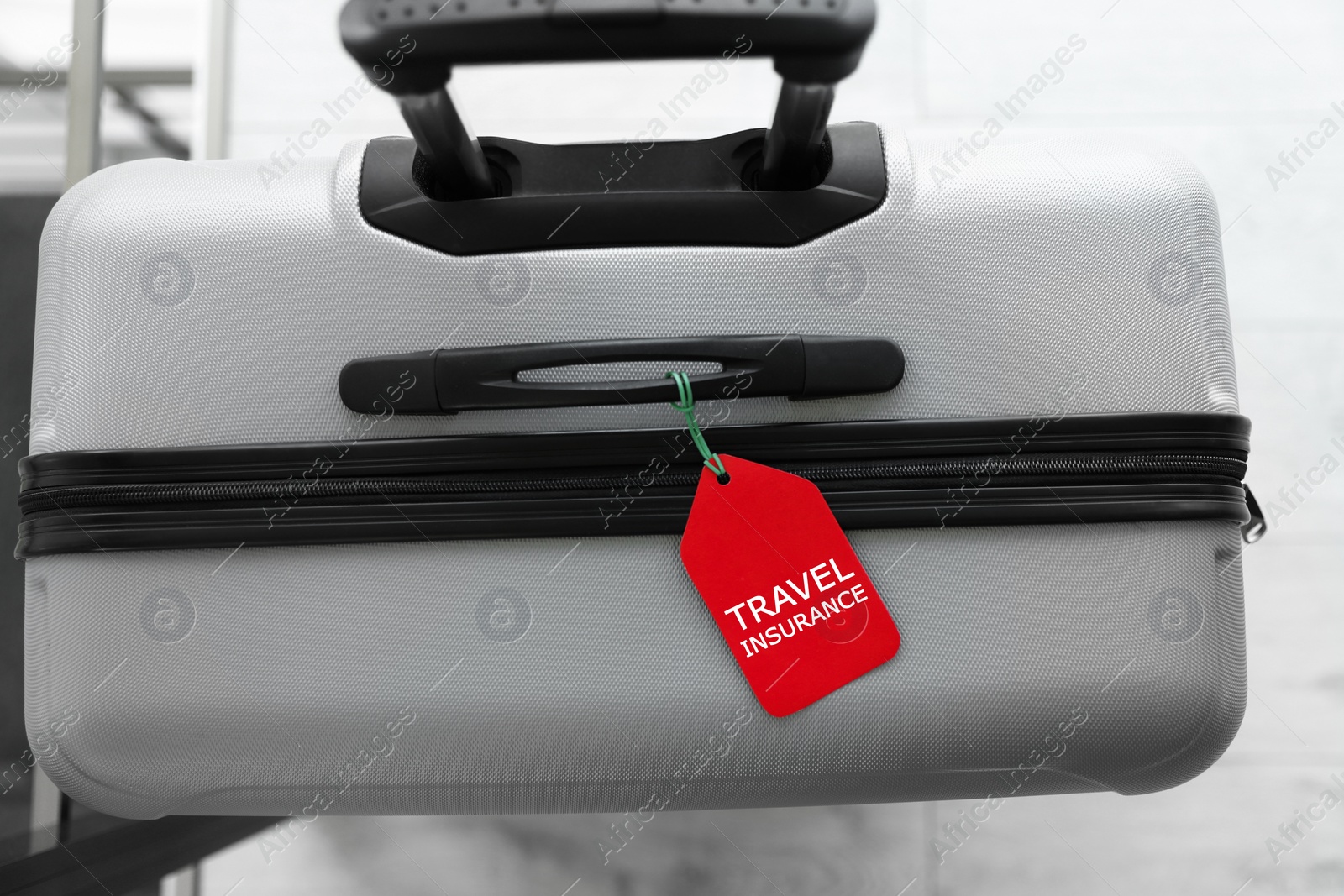 Photo of Stylish suitcase with travel insurance label on blurred background, closeup. Space for text