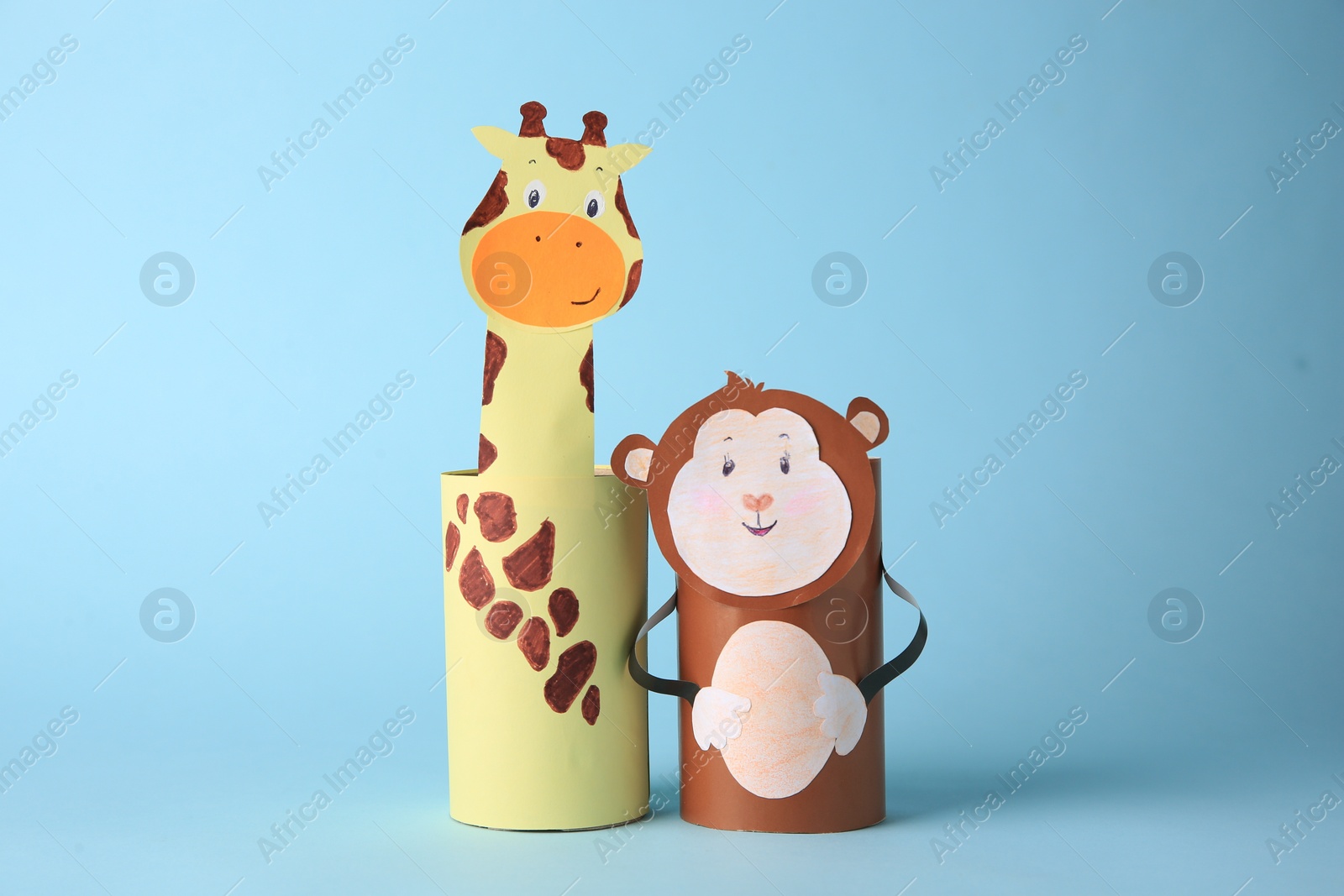 Photo of Toy monkey and giraffe made from toilet paper hubs on light blue background. Children's handmade ideas