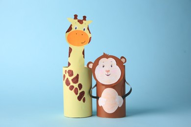 Photo of Toy monkey and giraffe made from toilet paper hubs on light blue background. Children's handmade ideas