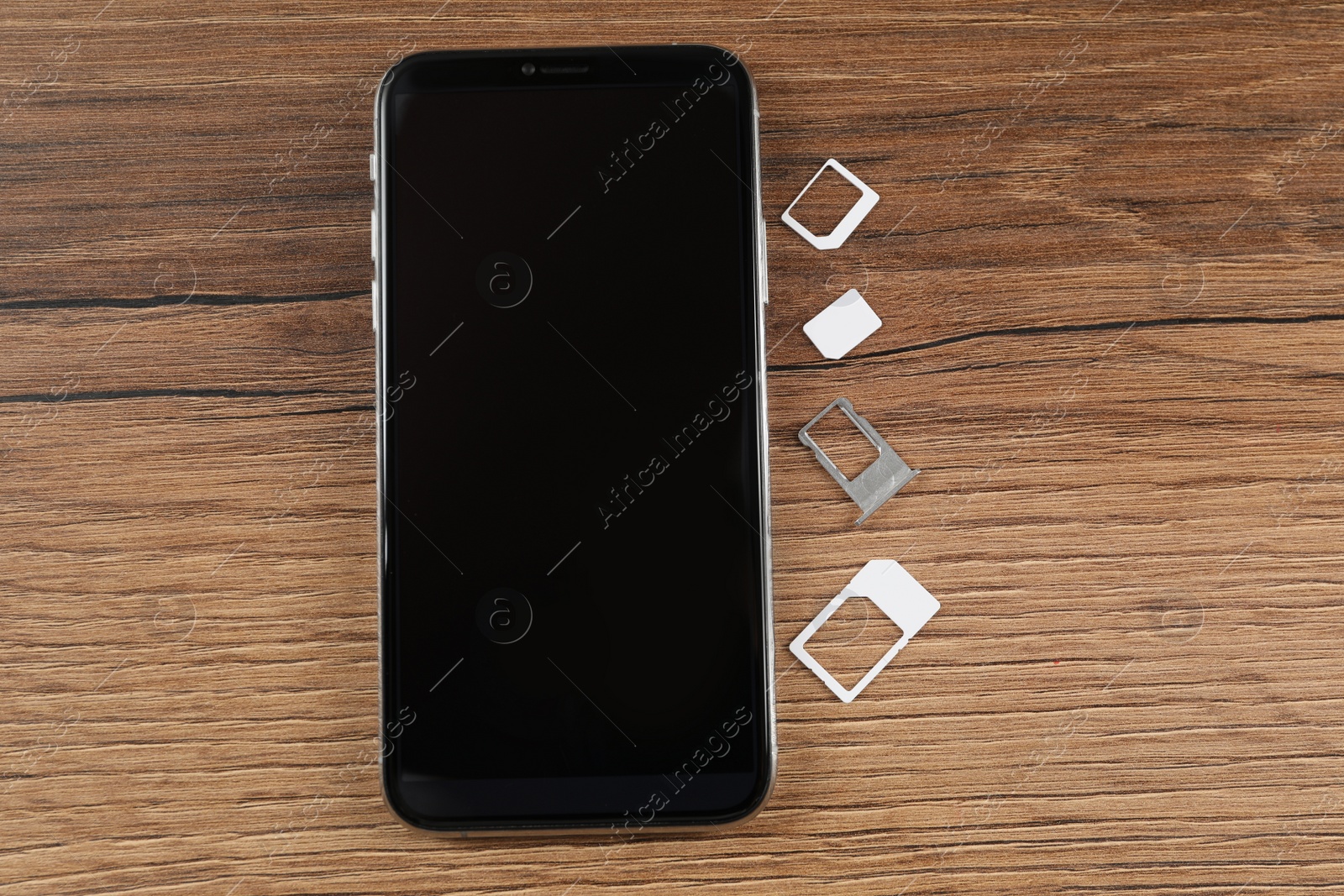 Photo of SIM card, tray and mobile phone on wooden table, flat lay