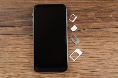 SIM card, tray and mobile phone on wooden table, flat lay