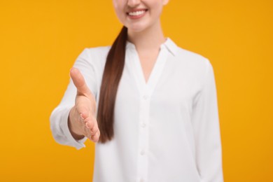 Photo of Smiling woman welcoming and offering handshake on orange background, closeup