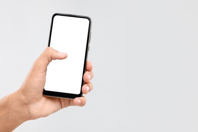 Man holding smartphone with blank screen on light grey background, closeup. Mockup for design