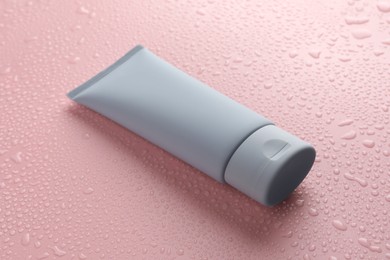Moisturizing cream in tube on pink background with water drops, closeup