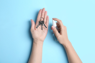 Photo of Woman spraying antiseptic onto keys on light blue background, top view