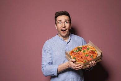 Attractive young man with delicious pizza on color background