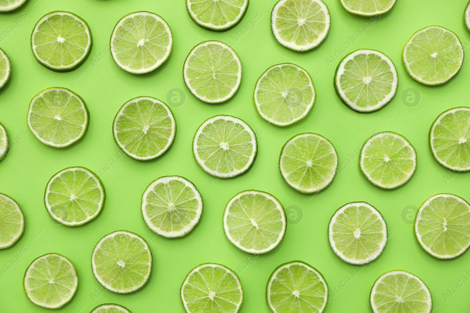 Photo of Slices of fresh juicy limes on green background, flat lay