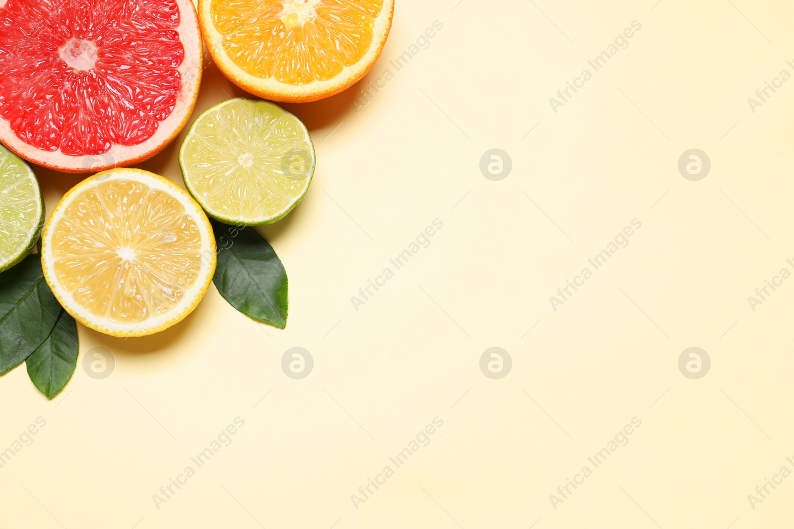 Photo of Different cut citrus fruits and leaves on beige table, flat lay. Space for text