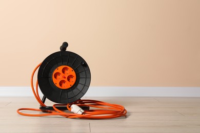 Photo of Extension cord reel on floor near pale pink wall, space for text. Electrician's equipment