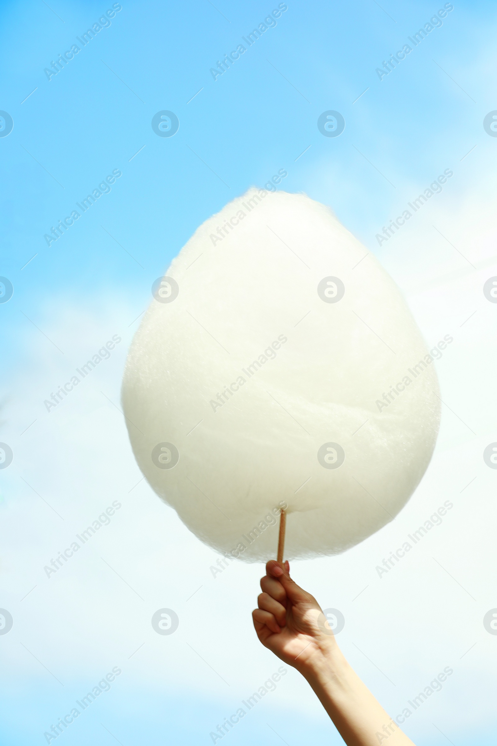 Photo of Woman holding white cotton candy against blue sky, closeup