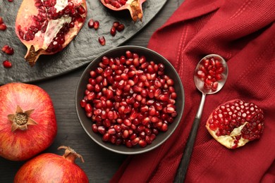 Photo of Tasty ripe pomegranates and grains on dark wooden table, flat lay