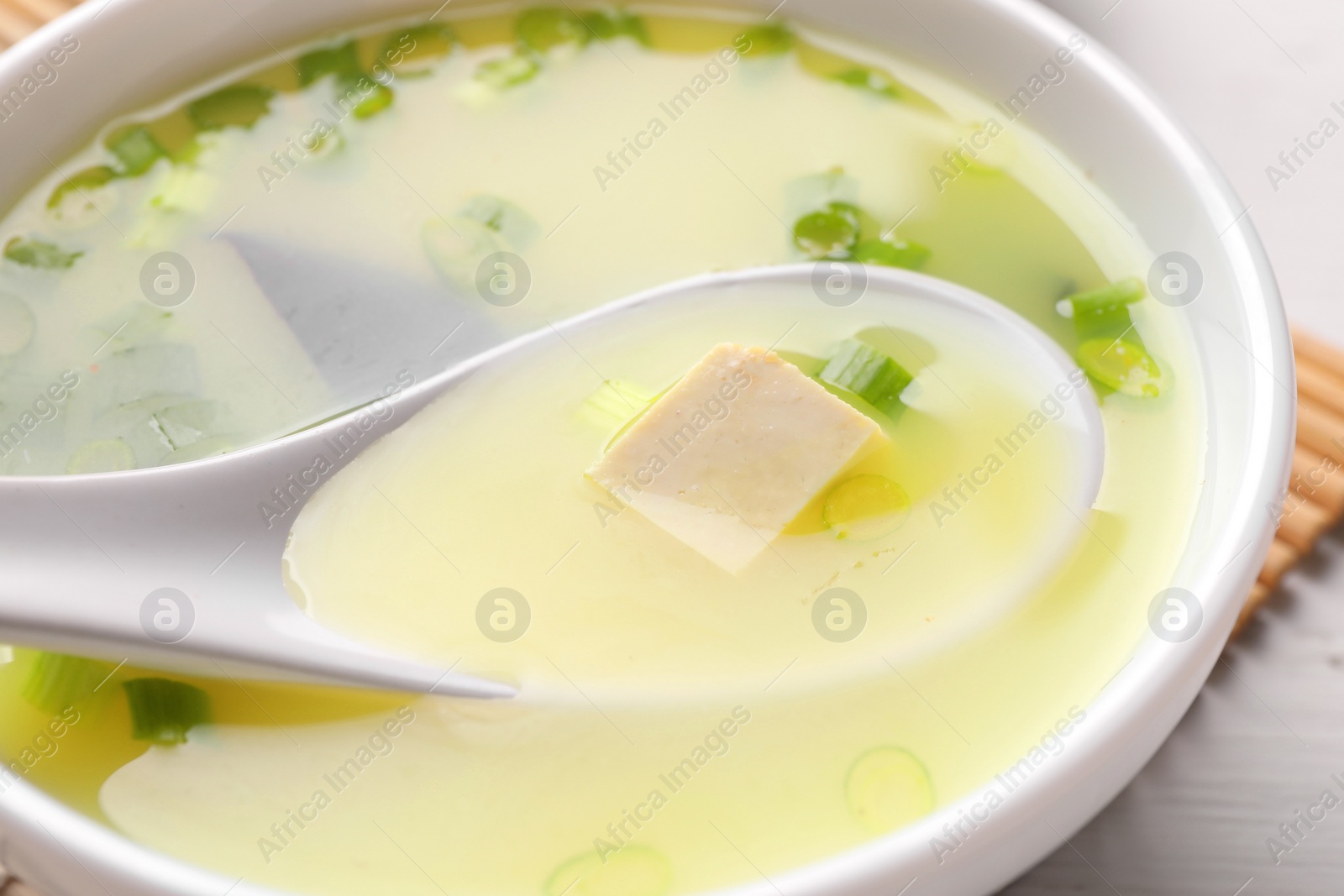 Photo of Bowl of delicious miso soup with tofu and spoon on table, closeup