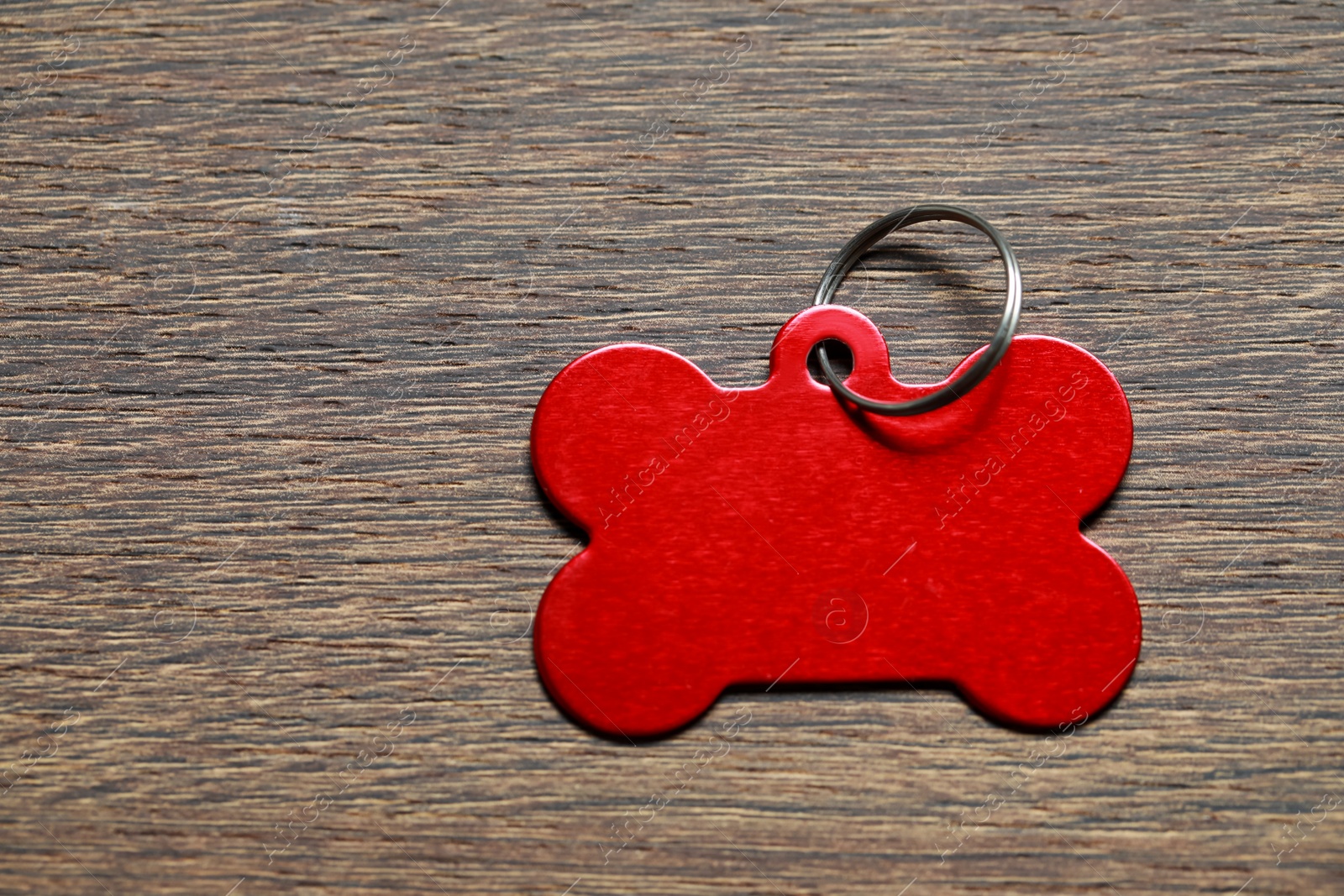 Photo of Red metal pet tag in shape of bone with ring on wooden table, top view. Space for text