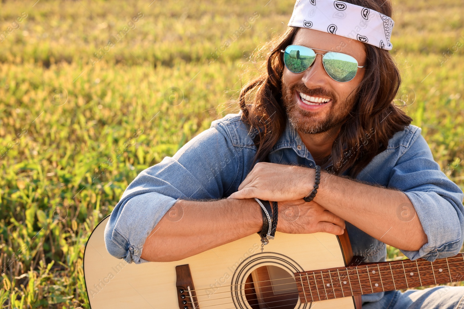 Photo of Portrait of happy hippie man with guitar in field