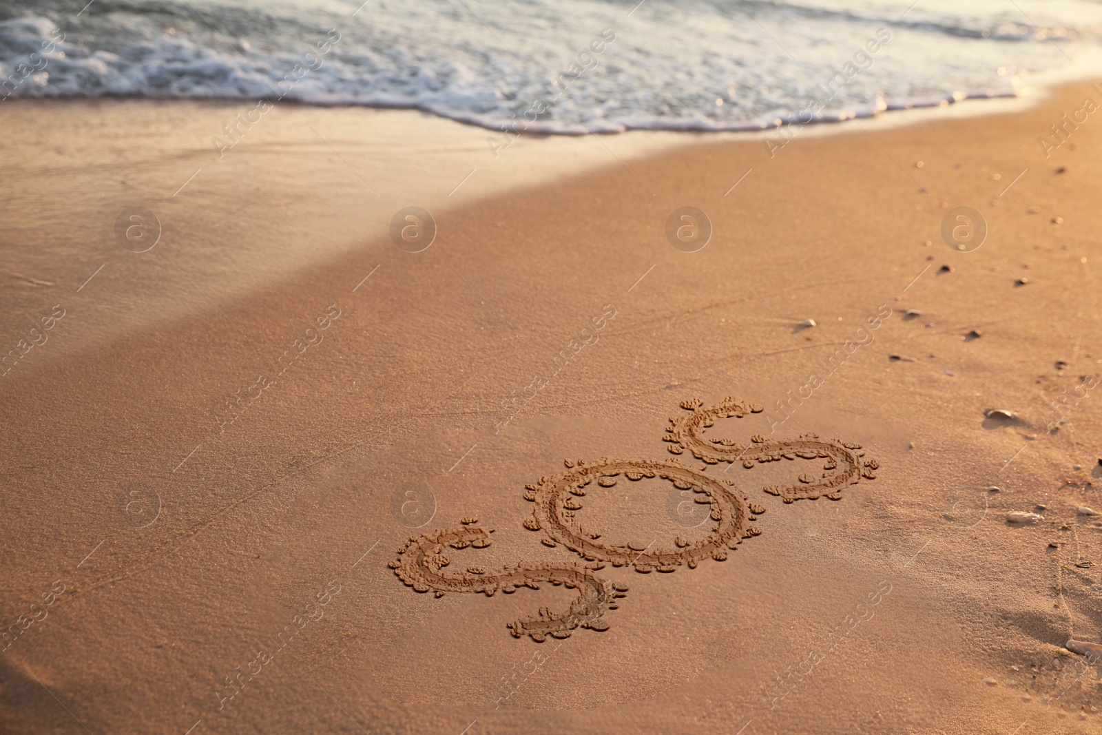 Image of SOS message drawn on sandy beach near sea