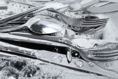 Washing silver spoons, forks and knives in foam, closeup