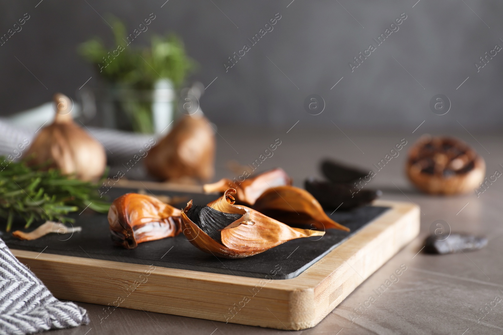 Photo of Board with black garlic on grey table. Space for text