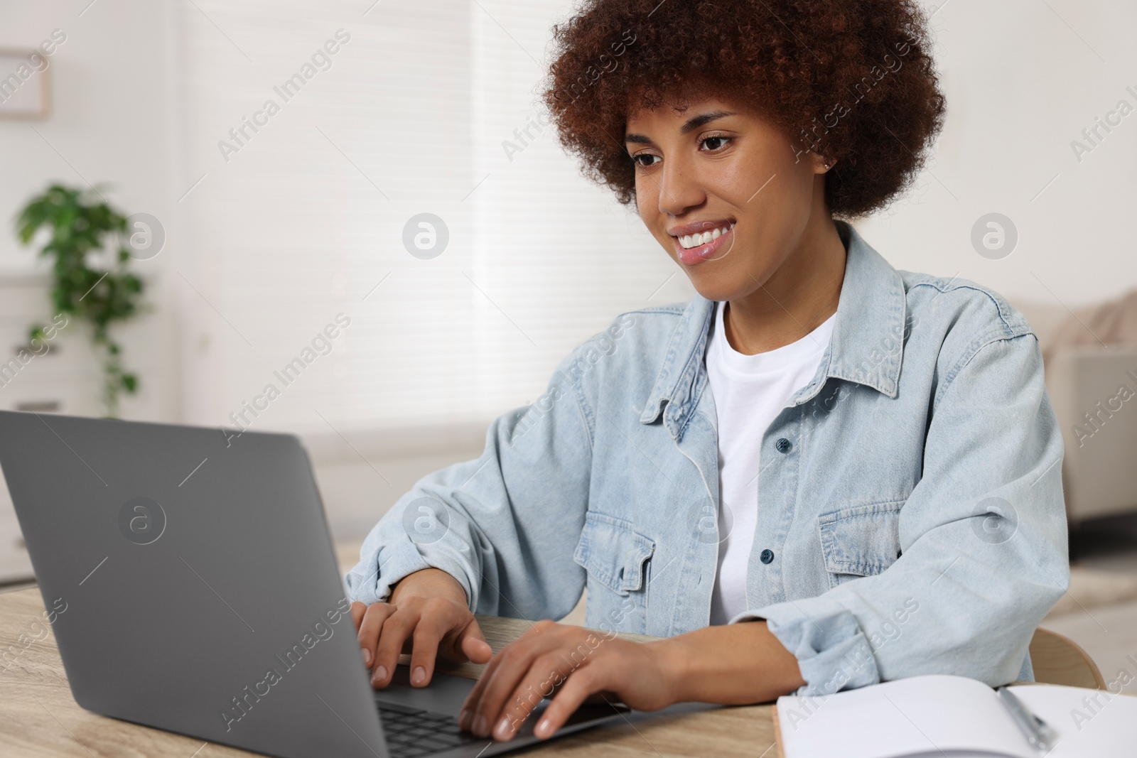 Photo of Young woman using laptop at wooden desk in room