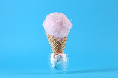 Photo of Sweet cotton candy in waffle cone on light blue background