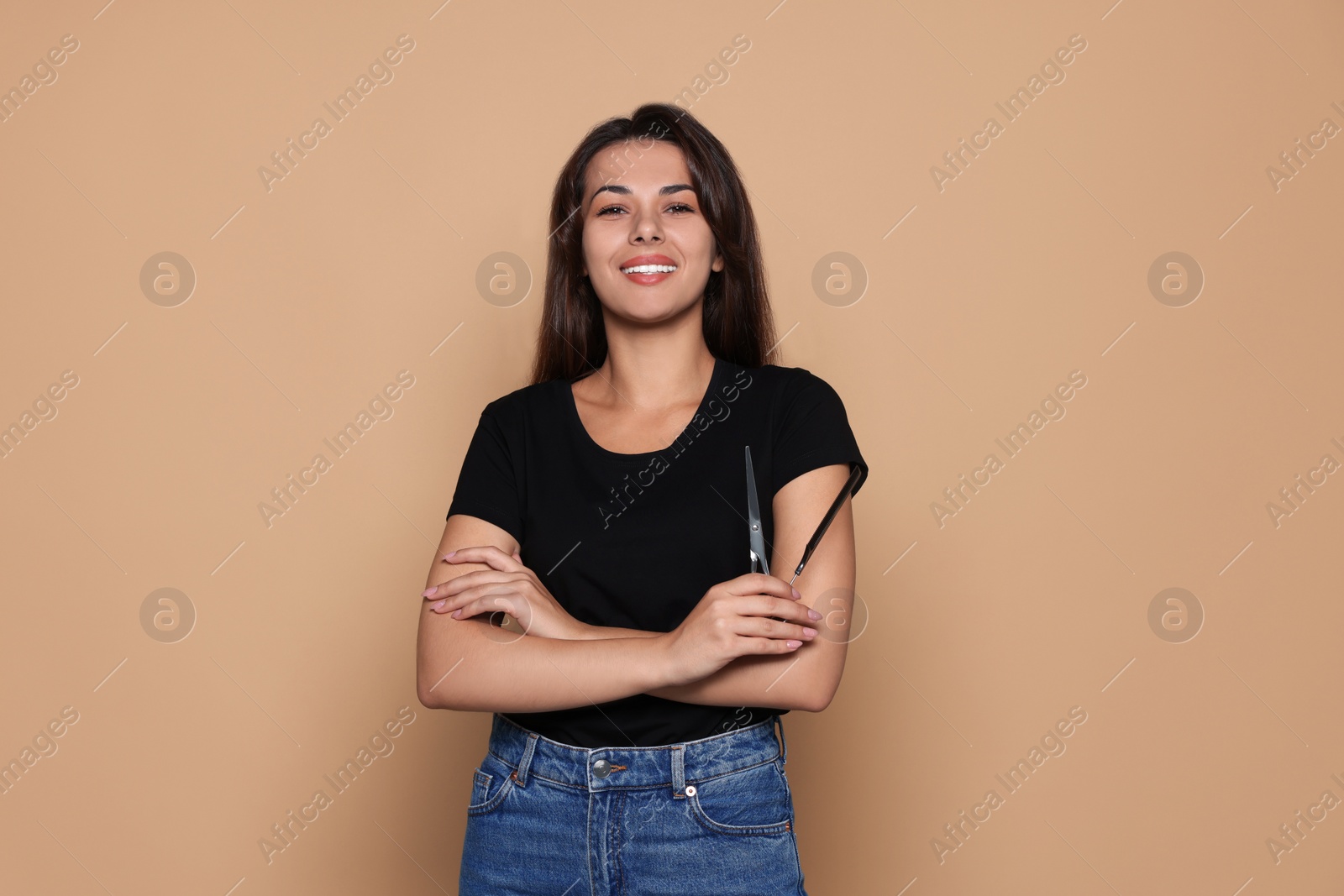 Photo of Happy professional hairdresser with scissors and comb against pale orange background