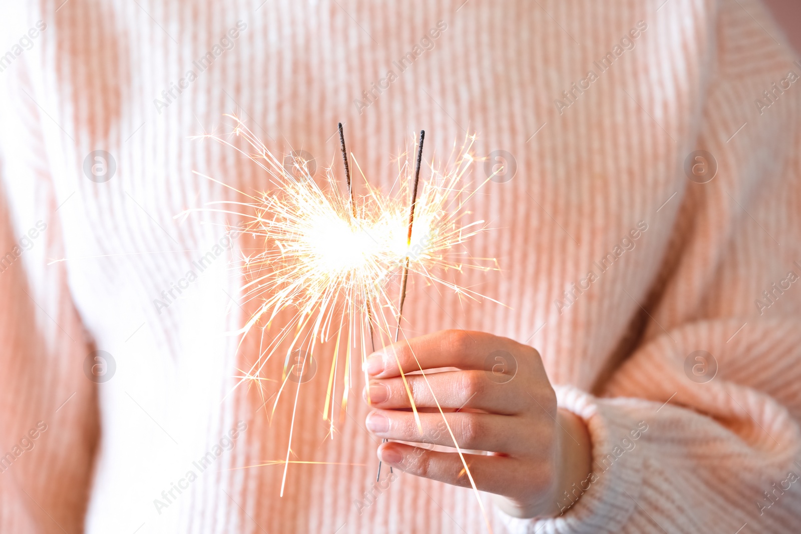 Photo of Woman in pink sweater holding burning sparklers, closeup