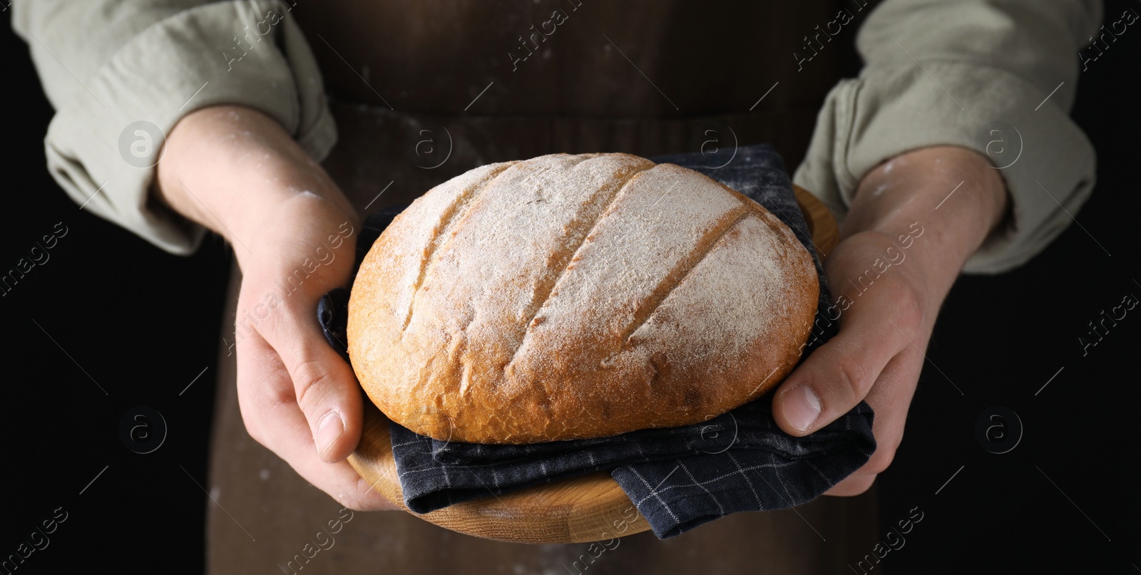 Photo of Woman holding freshly baked bread on black background, closeup