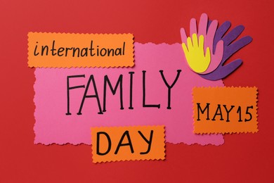 Photo of Paper palms and cards with text International family day on red background, flat lay