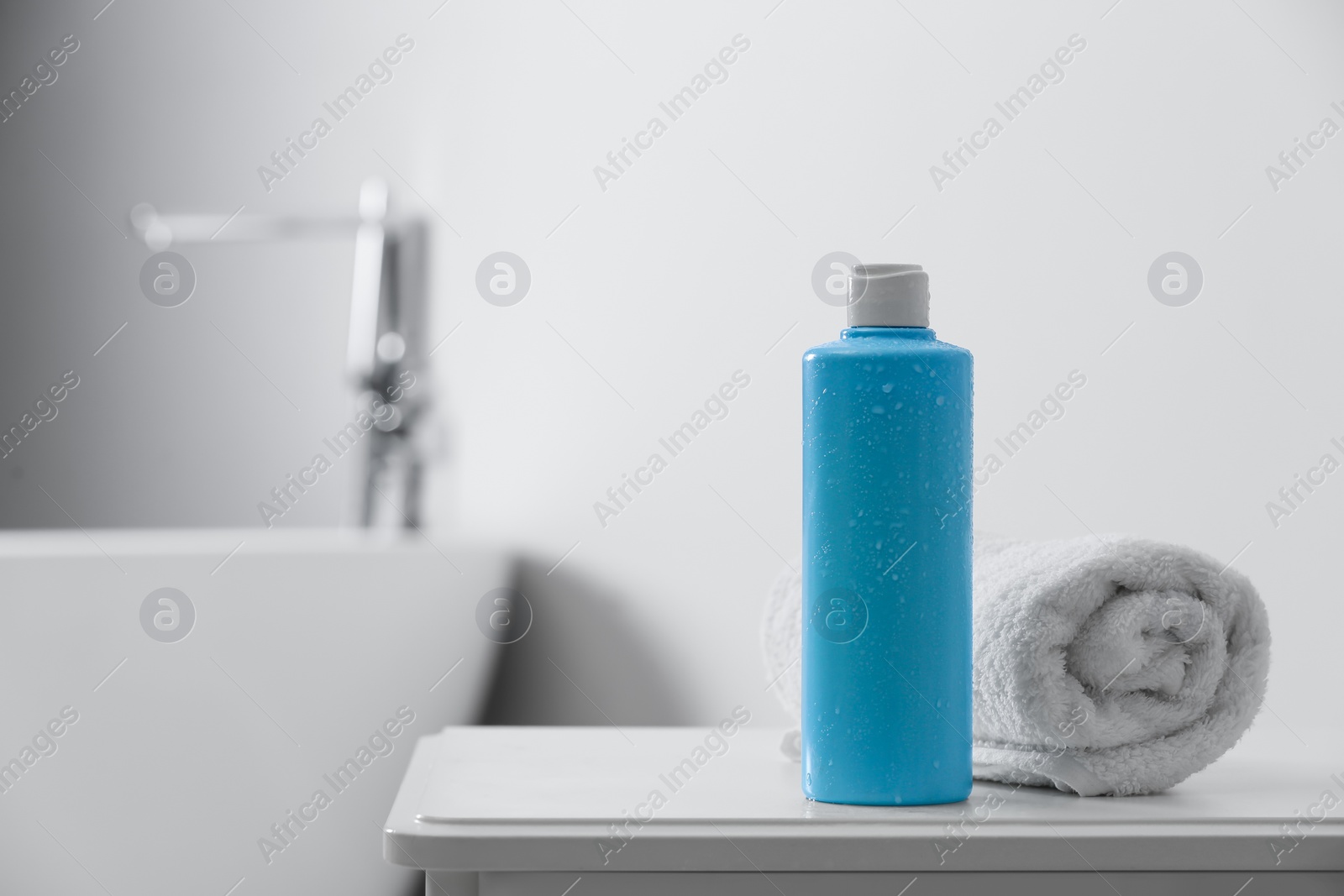 Photo of Bottle of bubble bath and towel on white table in bathroom, space for text
