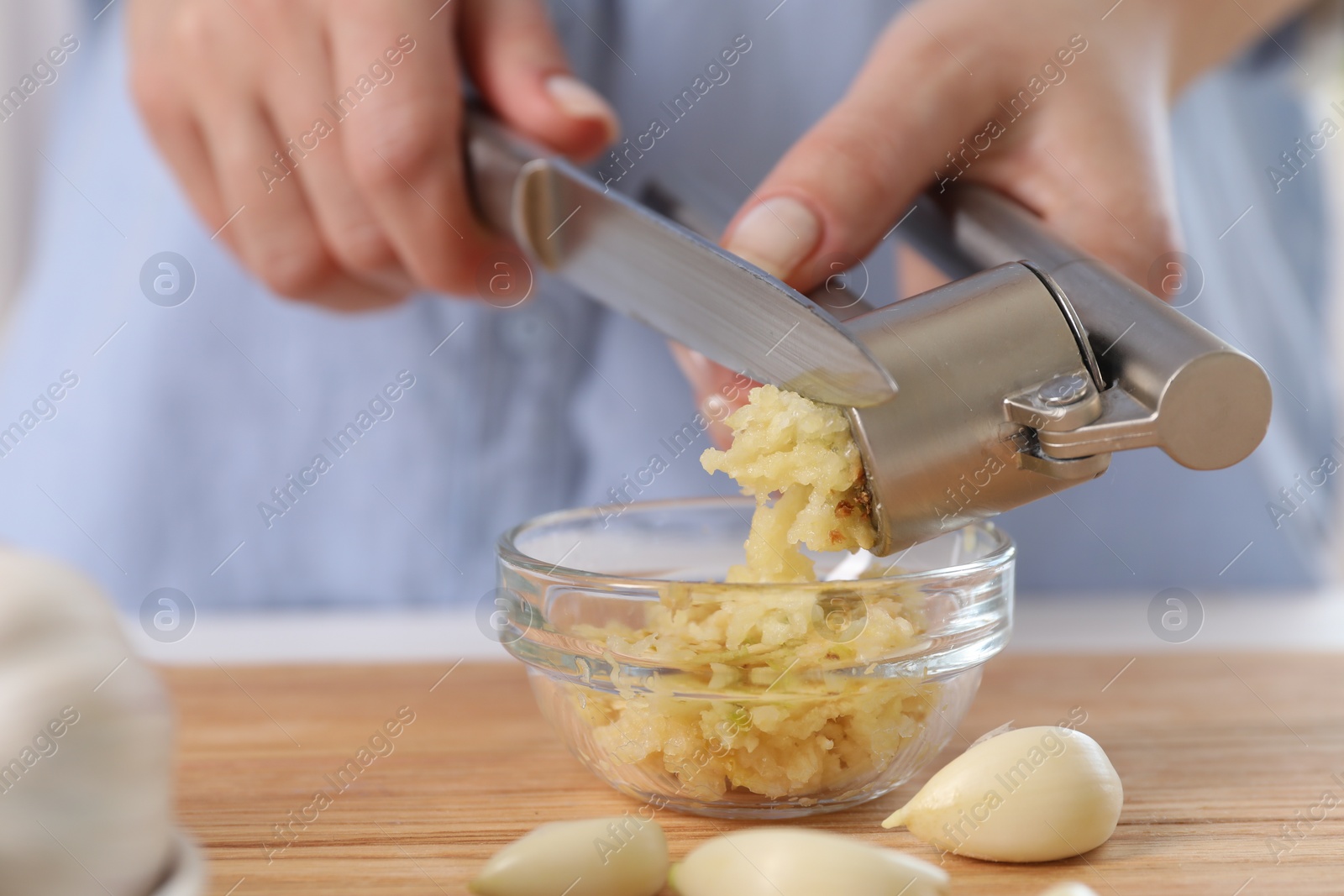 Photo of Woman squeezing garlic with press at wooden table, closeup