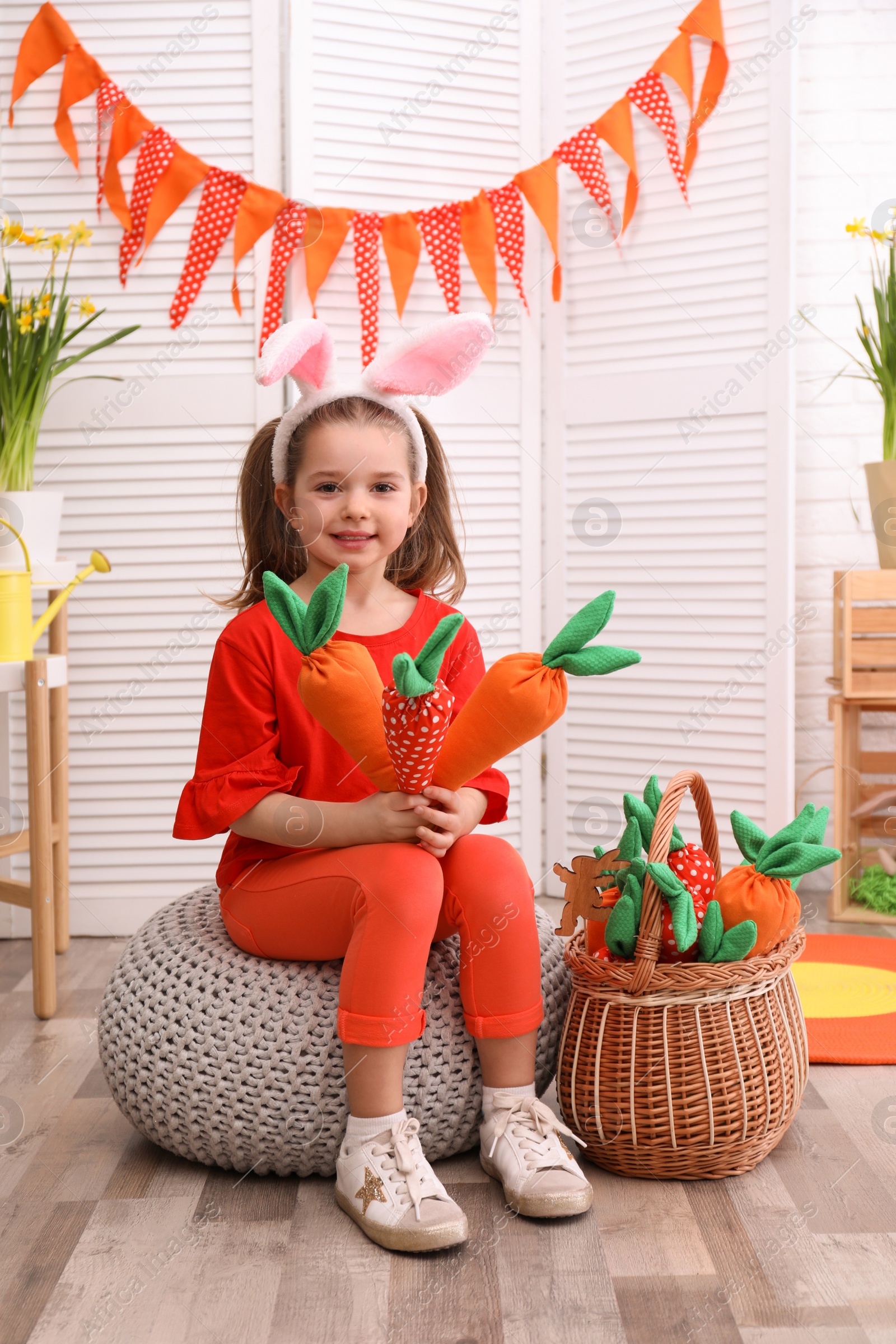 Photo of Adorable little girl with bunny ears and toy carrots in Easter photo zone