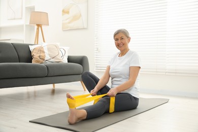 Senior woman doing exercise with fitness elastic band on mat at home