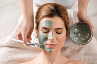 Photo of Cosmetologist applying mask onto woman's face in spa salon, top view