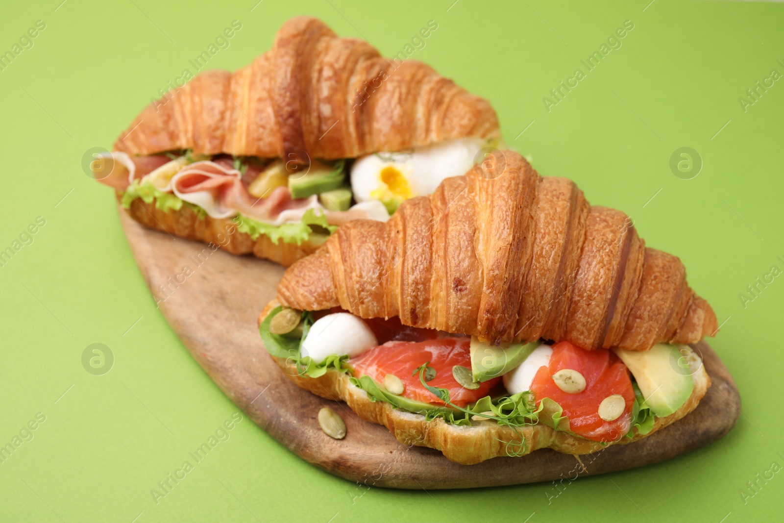 Photo of Delicious croissants with prosciutto and salmon on green table