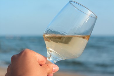 Woman holding glass of tasty wine near sea, closeup