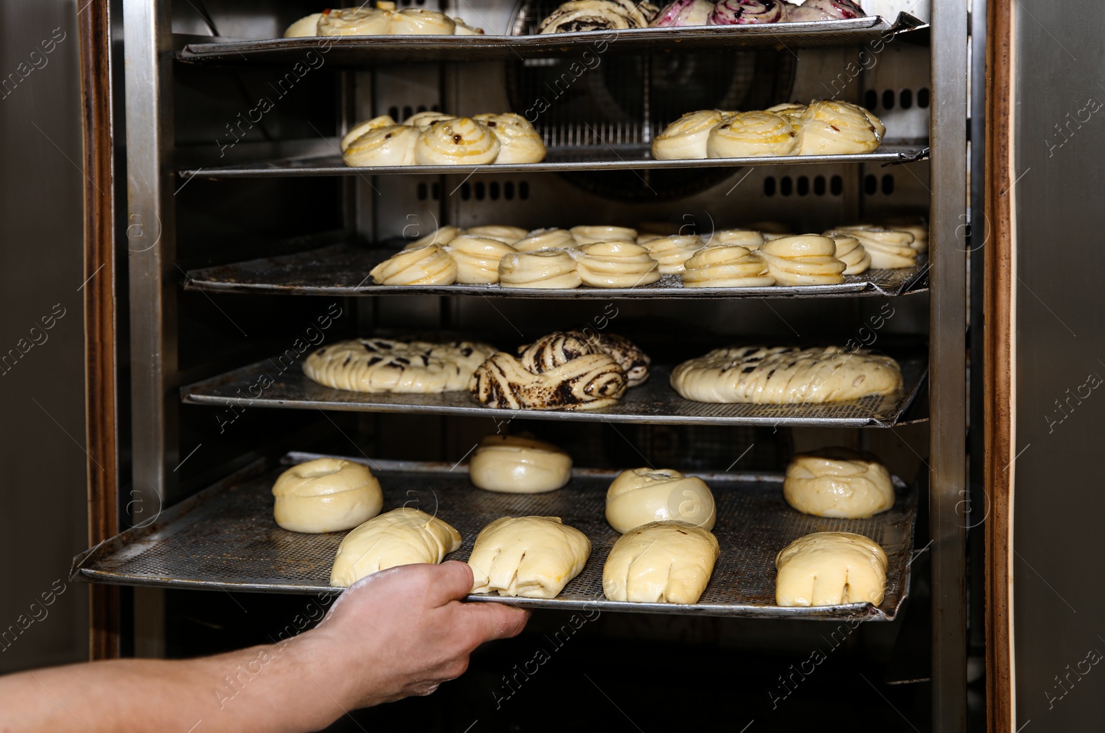 Photo of Baker putting tray with pastries into oven at workshop