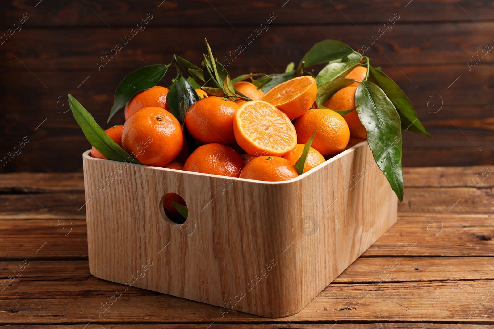 Photo of Fresh tangerines with green leaves in crate on wooden table