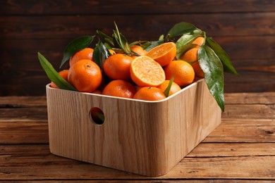 Fresh tangerines with green leaves in crate on wooden table