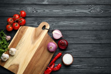 Cutting board and vegetables on black wooden table, flat lay with space for text. Cooking utensil