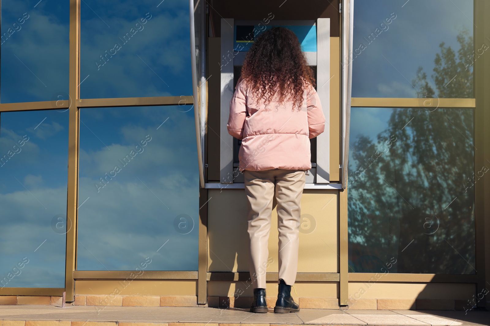 Photo of Young woman using modern cash machine outdoors, back view